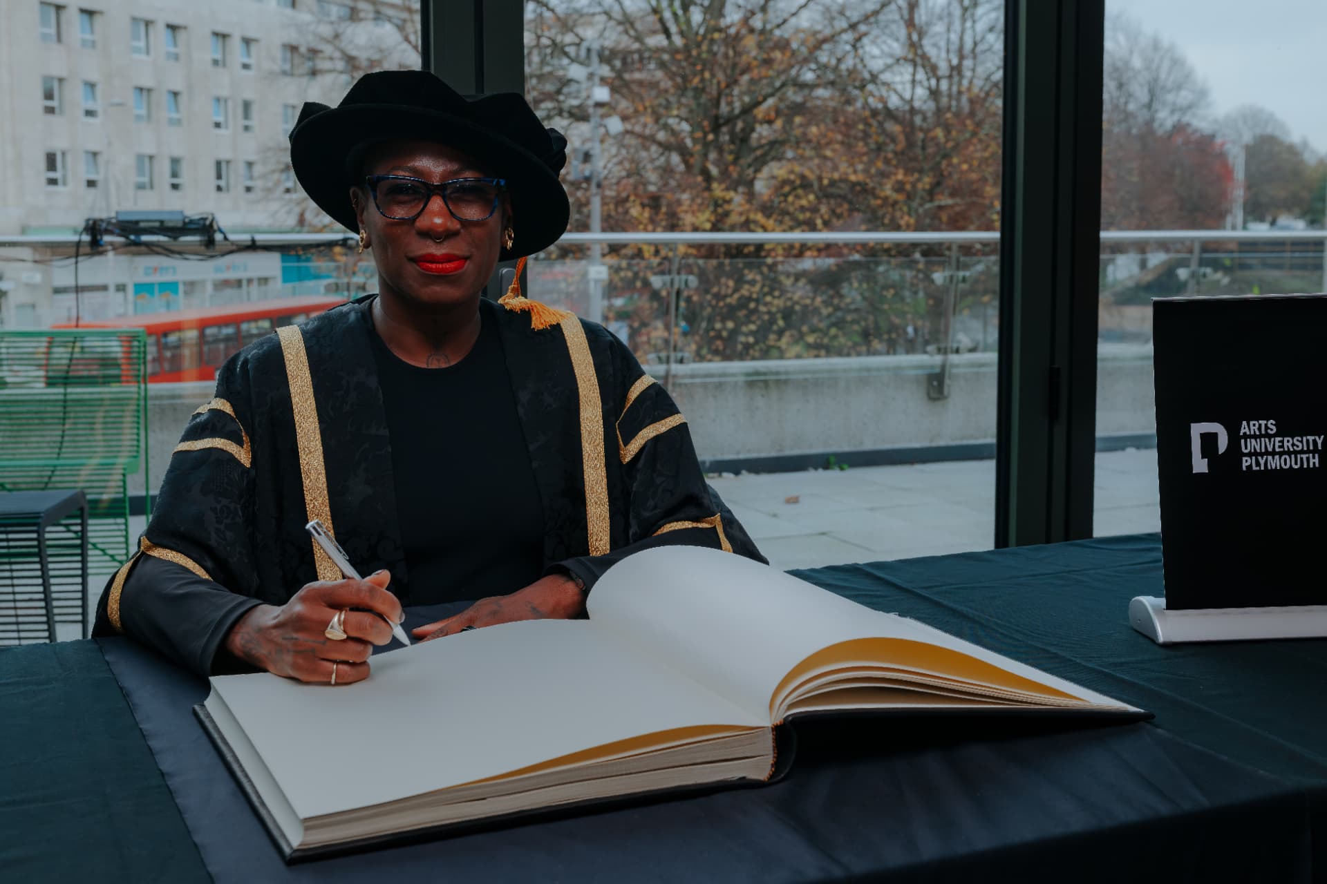 Ada Parris in academic robes signing the book at the Arts University Plymouth graduation