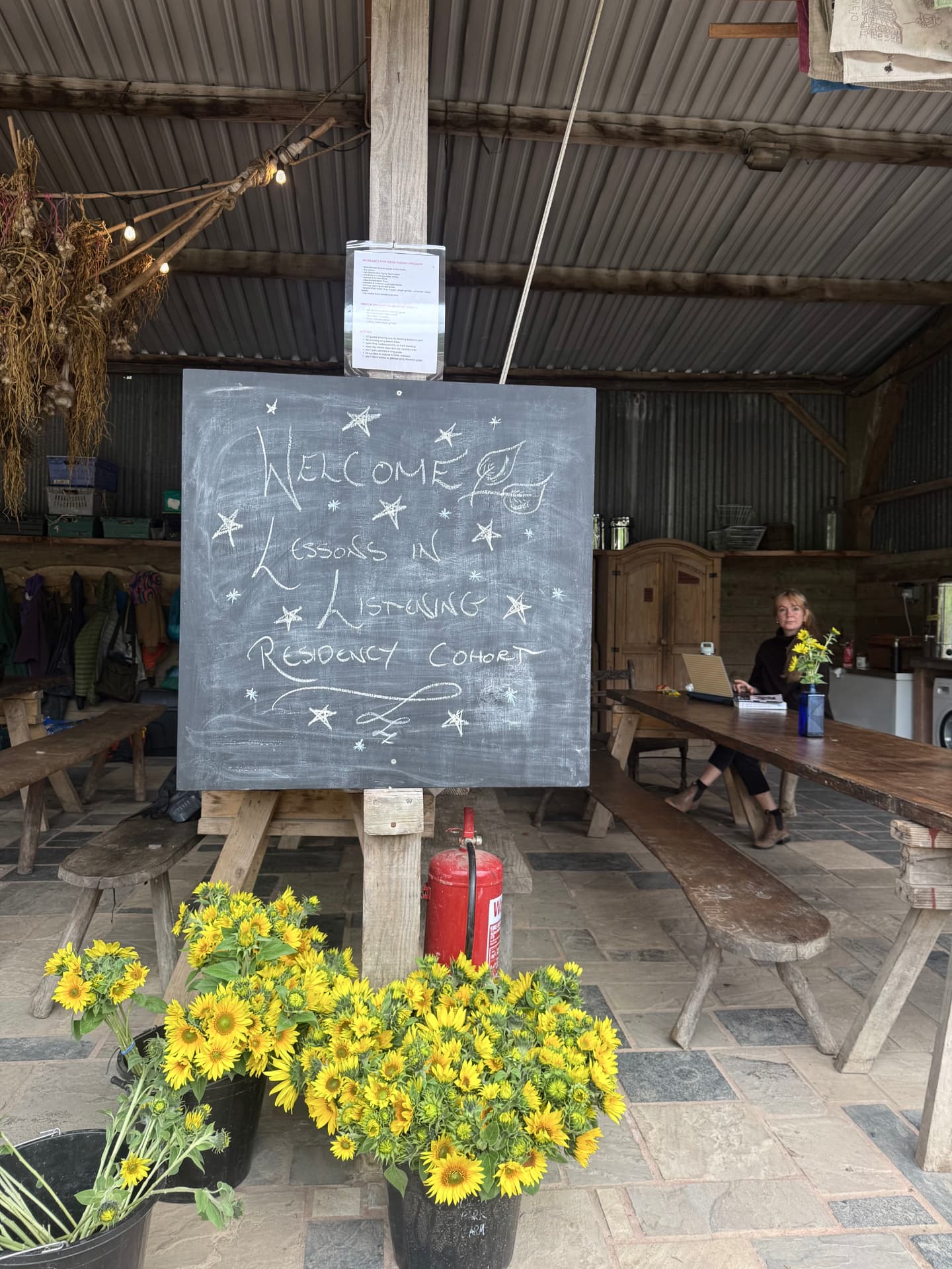 Chalkboard reading Welcome Lessons in Listening Residency Cohort, with sunflowers, in a barn on Dartmoor